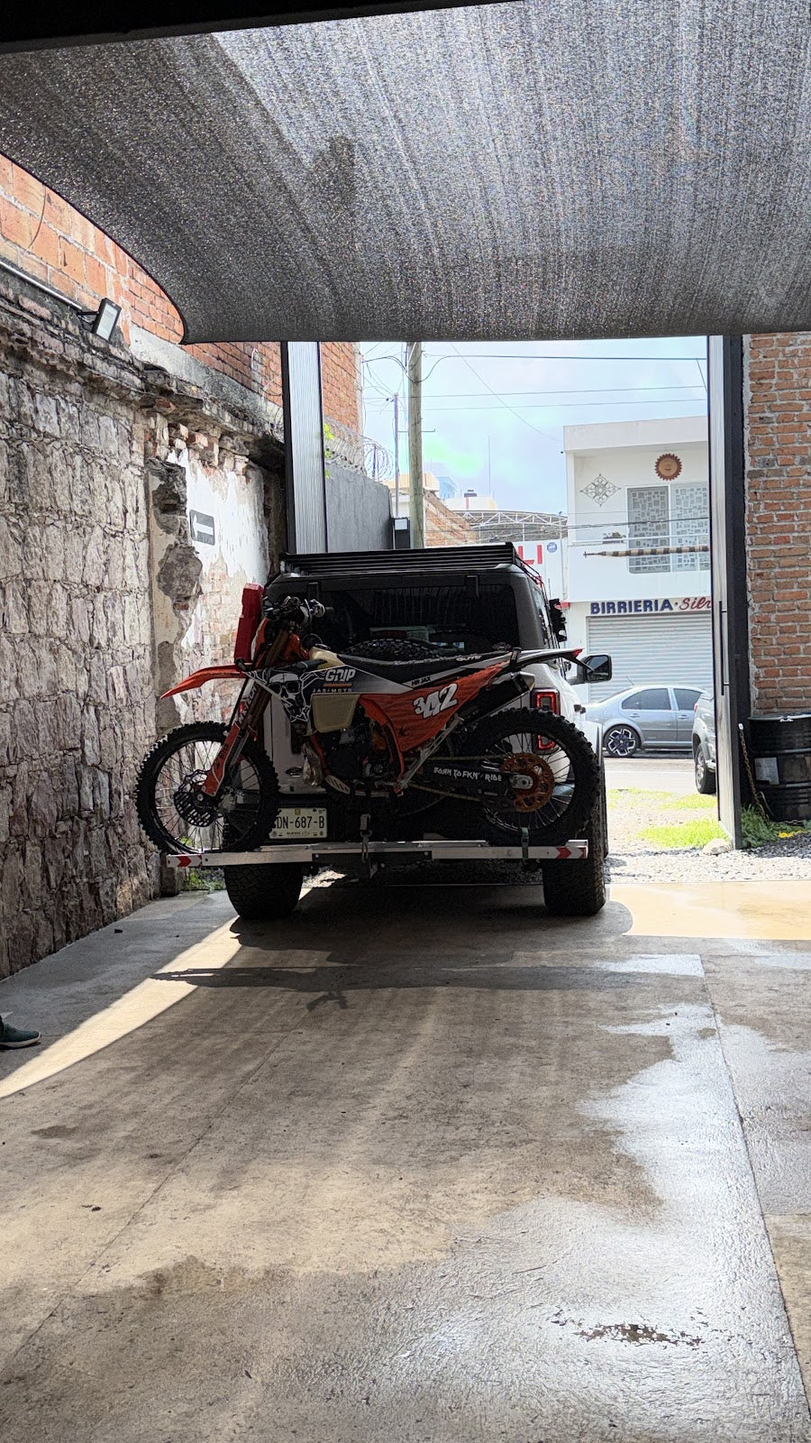 Acceso exterior techado de JAX Moto Lab con una moto y un vehículo